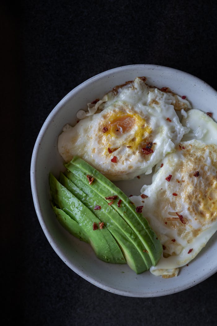 gallery-03 Top-down view of a breakfast bowl with fried eggs and sliced avocado, perfect for a healthy meal.